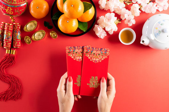 Chinese new year festival decorations. Woman hand holding pow or red packet, orange and gold ingots on a red background. Chinese characters FU means fortune good luck, wealth, money flow.