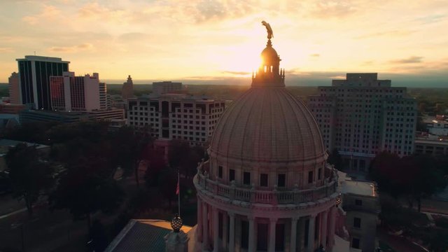 Aerial shot encircling the eagle from front to back of the Mississippi State Capitol buidling in Jackson Mississippi at sunset with city behind