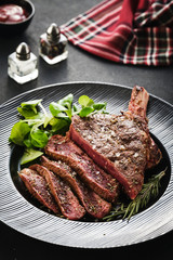 Steak on the bone. Rib eye. Tomahawk steak on the black plate with rosemary. Roasting - Rare. Entrecote