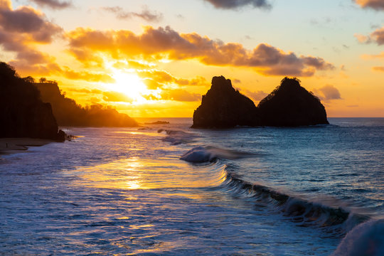 Beautiful sunset in Fernando de Noronha, Brazil. Taken from a mountain peak called Pedra do Bode. Waves crashing at shore with sun setting at distance near Two Brothers Mountain.