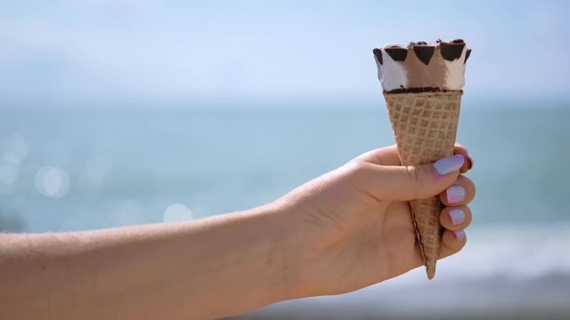 Close-up female hand holding refreshing ice cream cornet at bright sea background