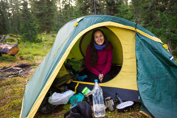 The girl is sitting in a tourist tent. Hiking in the mountains