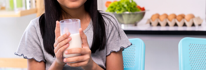 Portrait of a satisfied children holding glasses of milk in kitchen in morning. Cute little girl...