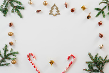 Christmas frame of fir branches and gold and brown Christmas tree toys, mint candy canes on white background, copy space. New year greeting card