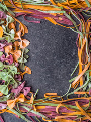 Frame of raw pasta, farfalle bow-tie, fettuccine or tagliatelle colorful pasta on grey background with flour, Colorful butterfly pasta. Italy ingredients for lunch.