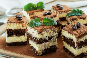 Pieces of tiramisu cake with delicate cream, coffee beans and mint leaves.