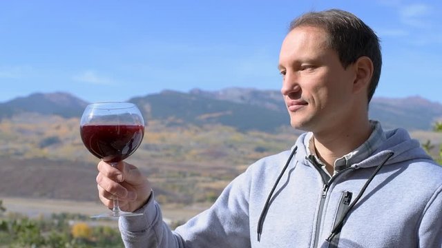 Young man standing in backyard garden at home drinking red wine from glass with view of rocky mountains in Aspen, Colorado in slow motion during autumn