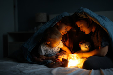 Magical three children and cat hide under blanket