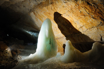 Inside the cave. Lighted section of the wall in the cave. Stalactites, stalagmites and ice growths inside the cave. - obrazy, fototapety, plakaty