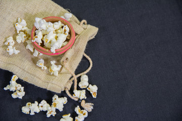 top view of popcorns with a traditional mud pot and mini popcorn jute bag on a black background