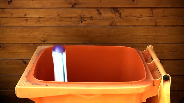 Slow motion shot of various household plastic items dropping into a recycle wheely bin.