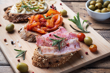 Wholegrain bread sandwiches with cream cheese, bacon and olives canned peppers with tomato on wooden background.