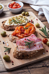 Wholegrain bread sandwiches with cream cheese, bacon and olives canned peppers with tomato on wooden background.