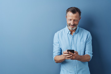 Middle-aged man reading an sms on his mobile - obrazy, fototapety, plakaty