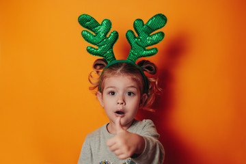 Christmas card with copy space. Little kid with green christmas antlers on head. Baby girl deer.