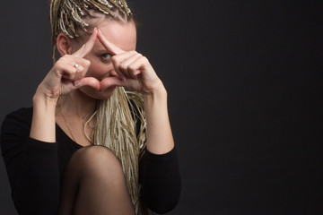 Studio portrait of a girl with dreadlocks afro hairstyle Zizi on a gray background holds fingers in...
