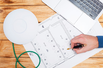 Engineering process. Man developing a network diagram for wifi access in cafe. Access point, floor layout, laptop and man hand on the bright background. Space for your text.