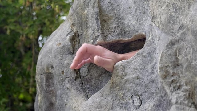 human hand comes out of gap in rock making grabbing action close-up.