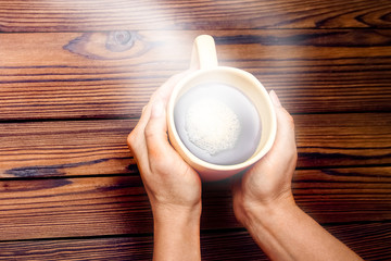 Female hands holding cup of coffee on wooden background