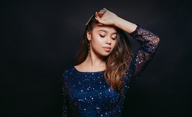 Young beautiful curly women in blue glitter dress on dark background. Copyspace. Concept celebration