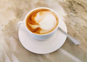 Typical Italian cappuccino espresso coffee breakfast on the marble counter of a bar. Typical cappuccino served in a white cup with spoon for mixing sugar