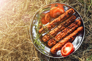 Sausages cooking on grill served on a plate with spices, herbs and tomatoes. Food background with barbecue party, top view - 307581355
