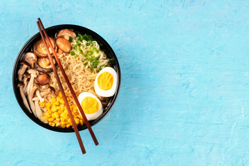 Ramen. Soba noodles with eggs, shiitake mushrooms, and vegetables, overhead shot on a blue background with chopsticks and copyspace