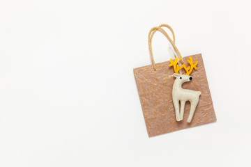 Golden Christmas gift bag, white felt toy deer with yellow horns on white background, copy space. Festive, New Year, sales, shopping concept. Horizontal, flat lay. Top view