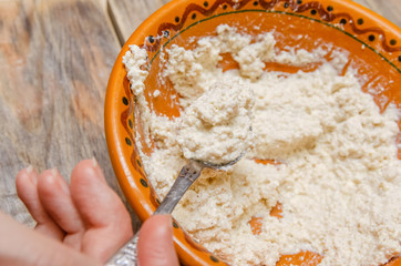 woman's hand holds a teaspoon of cottage cheese over a brown bowl of cottage cheese filling close up