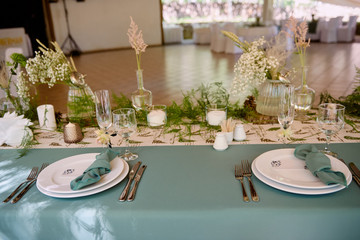 Table setting with blank guest card on empty white plate, turquoise serviette and cutlery on table, copy space. Menu mockup, place setting at wedding reception. Table served for wedding banquet
