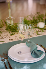 Table setting with blank guest card on empty white plate, turquoise serviette and cutlery on table, copy space. Menu mockup, place setting at wedding reception. Table served for wedding banquet