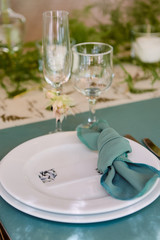 Table setting with blank guest card on empty white plate, turquoise serviette and cutlery on table, copy space. Menu mockup, place setting at wedding reception. Table served for wedding banquet