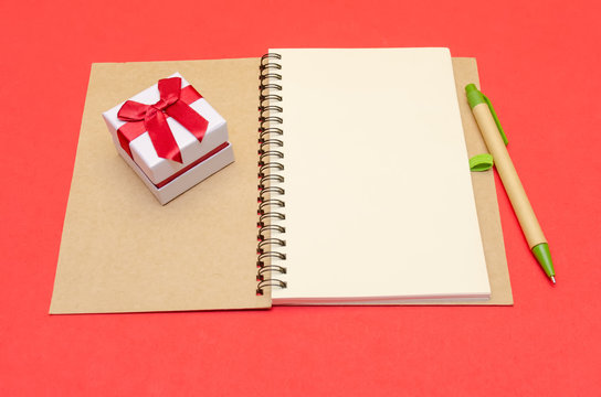 Notepad with pen and gift lies on a red background, copy space.