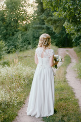 Fototapeta na wymiar Portrait of beautiful bride in long white wedding dress walking in garden at sunset, back view. Wedding concept, copy space