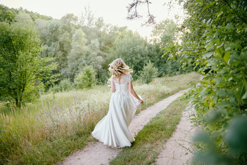 Portrait of beautiful bride in long white wedding dress walking in garden at sunset, back view. Wedding concept, copy space