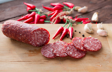 Smoked sausage sliced into pieces, slices of garlic and red chili peppers on a dark background. Not a healthy diet. The concept of cooking.