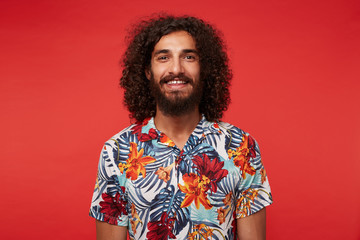 Portrait of pretty young brunette man with lush beard and curly hair looking joyfully to camera...