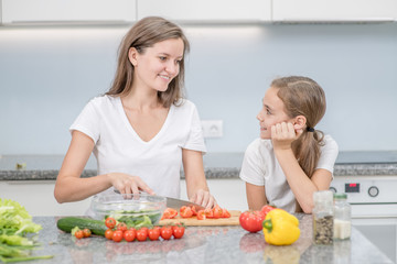 Happy mom and her daughter cook dinner in the kitchen