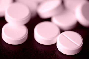 Round pharmaceutical pills scattered on a dark surface close-up. Pink color toned