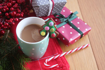 Christmas cookie in shape of a Christmas tree on a coffee cup on wooden table with decorations and gifts