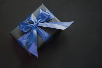 Gift box wrapped in black paper with classic blue ribbon on black surface.