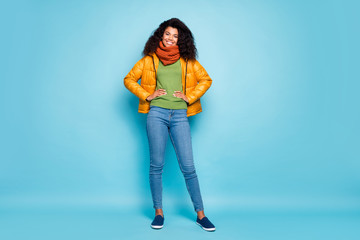 Full length photo of pretty dark skin curly lady in good spring mood going outside for walk traveler wear trendy yellow fall overcoat jeans green pullover isolated blue color background © deagreez