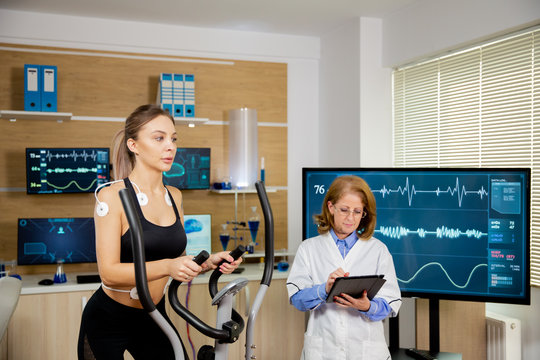 Female athlete testing the stepper with electrodes on her and the doctor making notes in the tablet