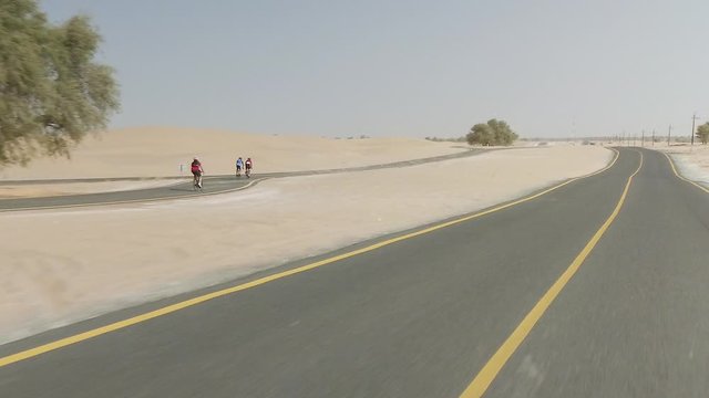Tracking shot of three cyclists cycling on a desert track in Al Quadra Dubai United Arab Emirates