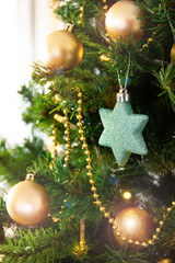 Close up of blue star shaped ornament on christmas tree with golden ornaments and lights