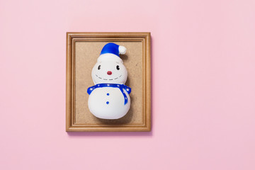 cheerful snowman in a brown frame on a pink background