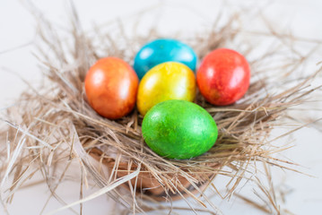 Fototapeta na wymiar Multi-colored Easter eggs lie on a straw in the form of a nest in a basket on a white background. Happy easter