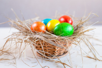 Multi-colored Easter eggs lie on a straw in the form of a nest in a basket on a white background. Happy easter