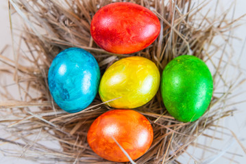 Multi-colored Easter eggs lie together on a straw in the form of a nest on a white background. Happy easter