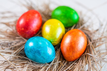 Multi-colored Easter eggs lie together on a straw in the form of a nest on a white background. Happy easter